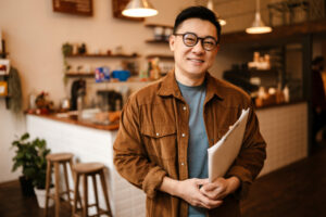 Adult asian man smiling and holding paper documents in cafe indo